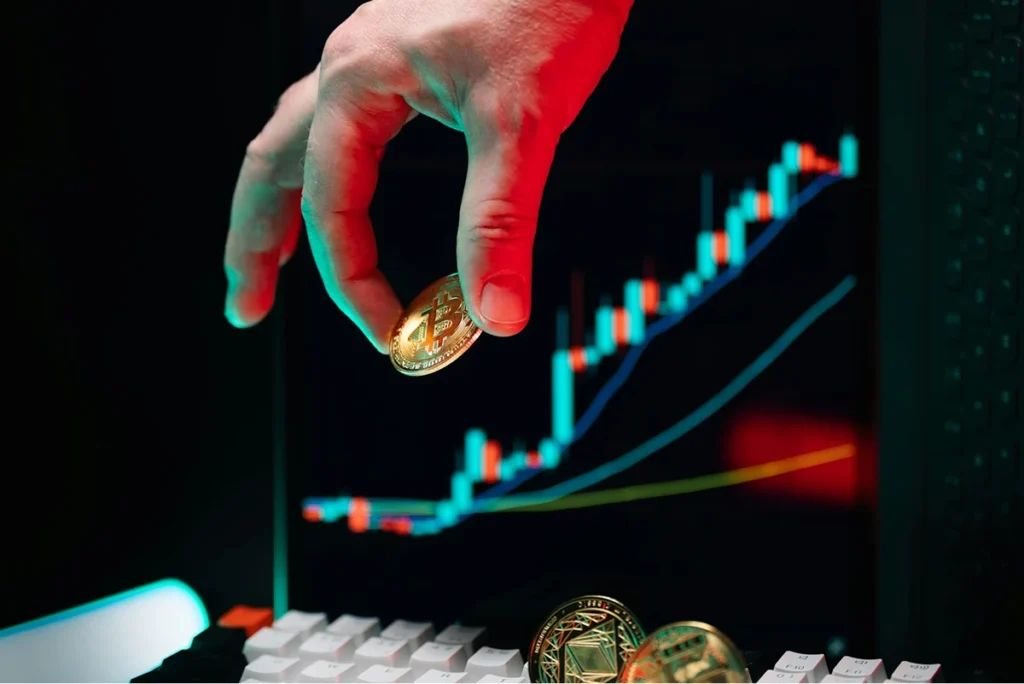 A hand holds a cryptocurrency coin, with a stock market chart displayed on a screen in the background, representing the world of banking and finance, including digital assets.
