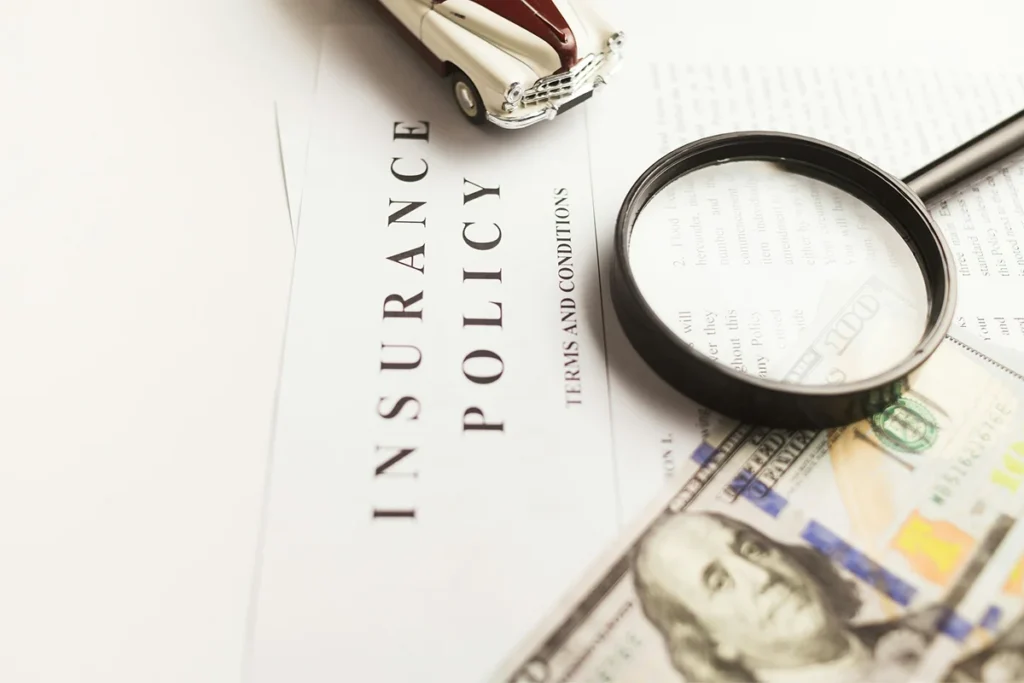 This image features an insurance policy document, a magnifying glass, and a toy car, symbolizing the detailed scrutiny and financial aspects of the insurance industry.